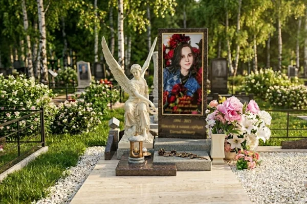 Эстетичный мемориальный комплекс из гранита с портретом девушки, статуей белого ангела и розовыми цветами на фоне березовой рощи.